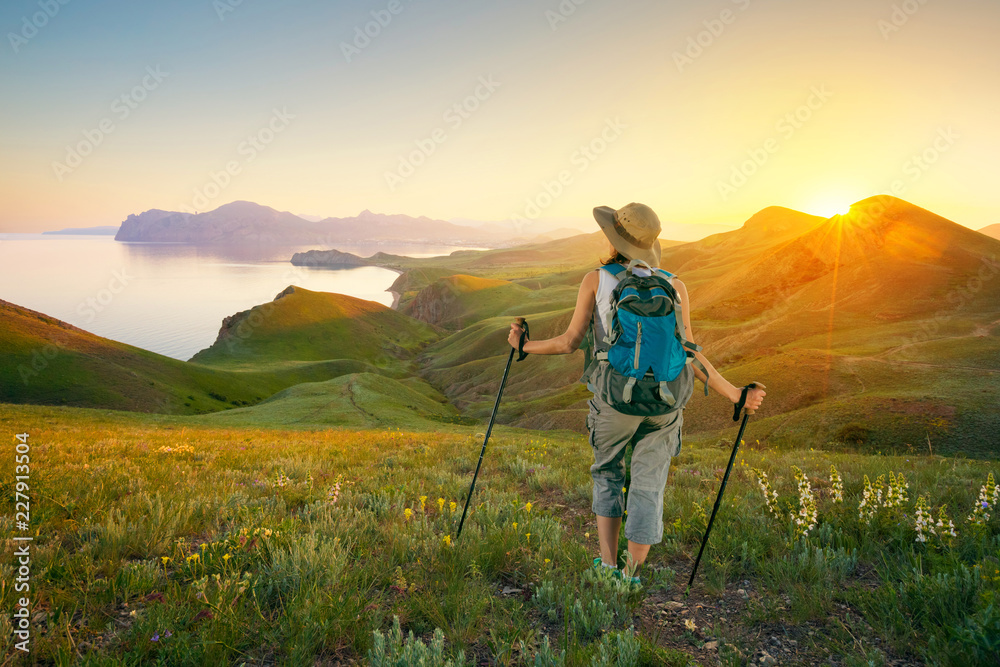 Hiking in the mountains. Woman backpacker looks at mountain seascape sunset.