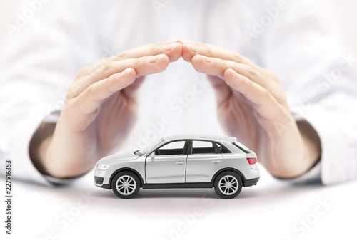 Car insurance. Small silver car covered by hands.