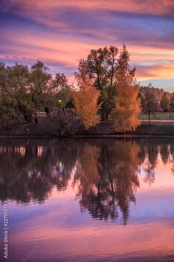 Obraz premium Autumn landscape. Fantastic dramatic colorful flaming sky, trees and reflections in the lake after sunset in the park. Autumn in Moscow parks, Russia.
