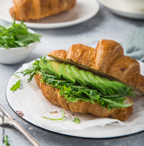 croissant sandwich with avocado, arugula and fried egg for breakfast, selective focus