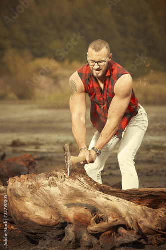 Fitness tattooed bodybuilder with double edge axe outdoor in sunny day