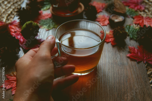 Female hands holding cup of tea with over wooden autumn background with leaves.  Autumn lifestyle concept 
