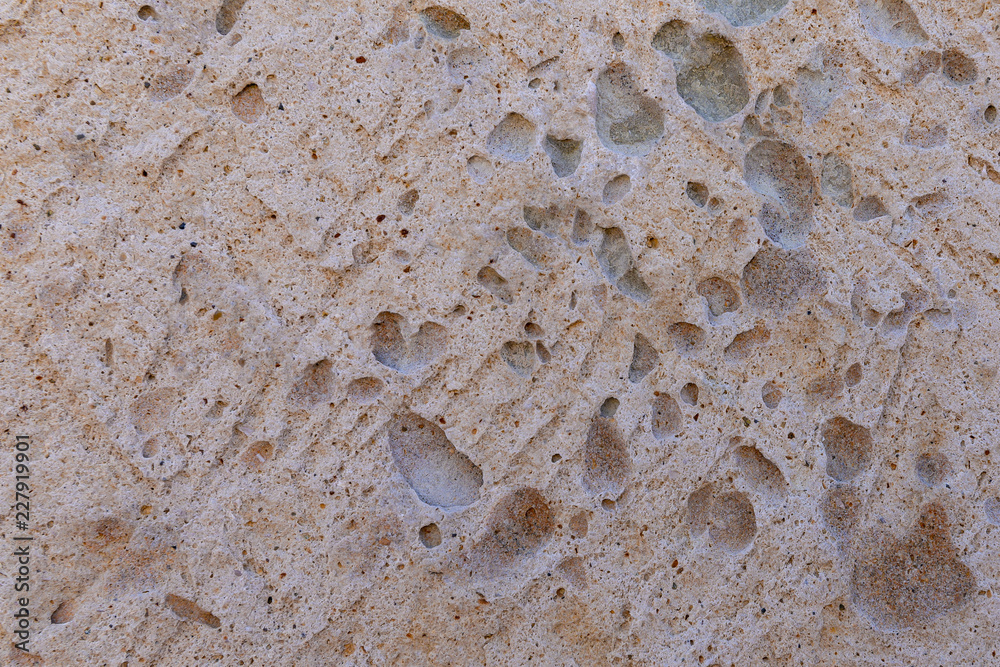 Background of beige textured limestone . Pocketed rough surface with dark inclusions Background of beige textured limestone . Pocketed rough surface with dark inclusions