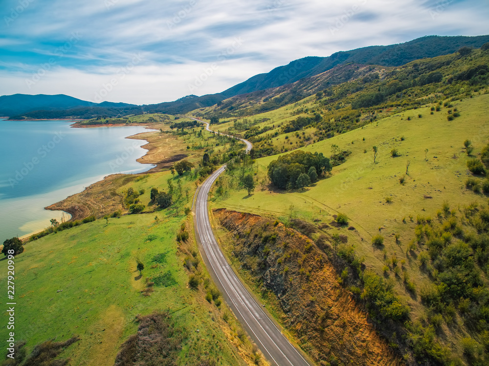 Rural road winding through lake shore and mountains. Scenic aerial landscape of Australia