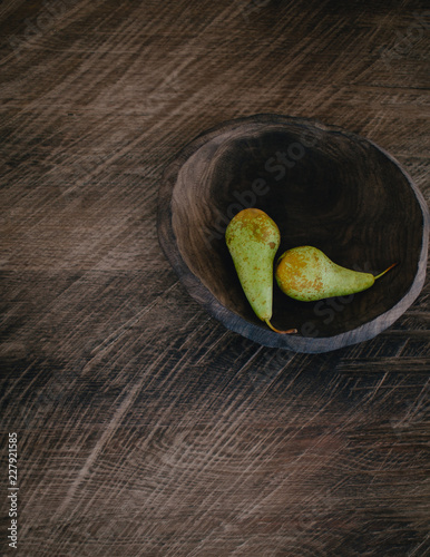 Two pears in a wooden plate on a wooden table
