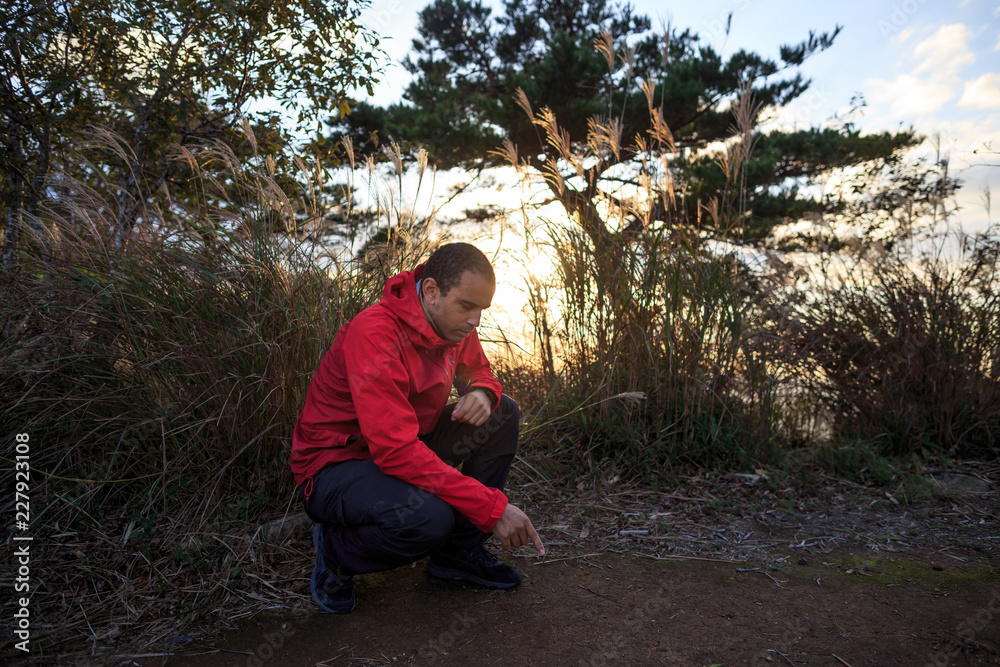 Man crouched, pointing at ground in front of tall grass and beautiful sunset Man crouched, pointing at ground in front of tall grass and beautiful sunset