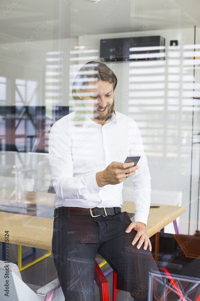 Fototapeta premium Happy young man using his smart phone at office