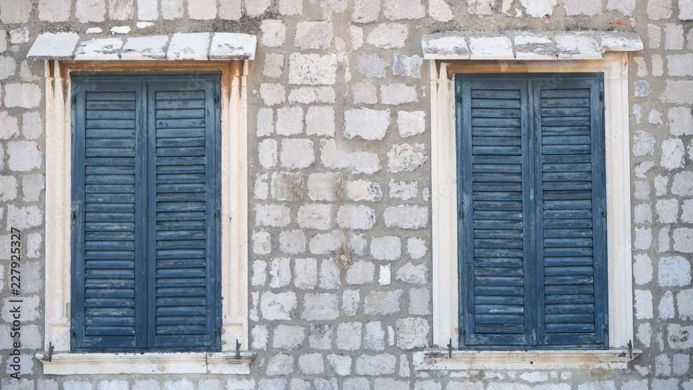 Two windows in old wall with closed blue shutters