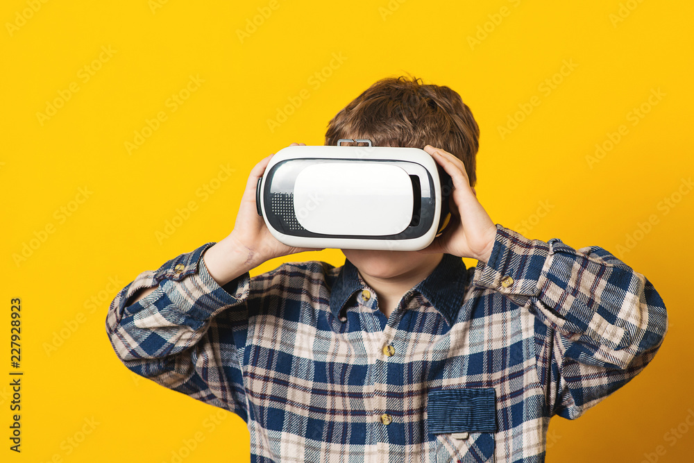 Kid wearing virtual reality glasses, isolated on yellow. Future technology. Boy using a virtual reality headset. Modern technology, gaming and people concept. Child in 3d glasses playing video game. Kid wearing virtual reality glasses, isolated on yellow. Future technology. Boy using a virtual reality headset. Modern technology, gaming and people concept. Child in 3d glasses playing video game.