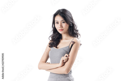 Cheerful young woman wearing light dress standing and posing on isolates white background.Lady flicking holding make up brush. © Suthiporn