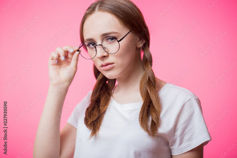 Close up portrait of young attractive girl with glasses and looking at camera on pink background Close up portrait of young attractive girl with glasses and looking at camera on pink background