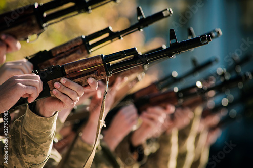 Many army soldiers in a row holding guns and rifles and shooting in same direction in the air closeup bokeh background. Concept of military conflict and celebration