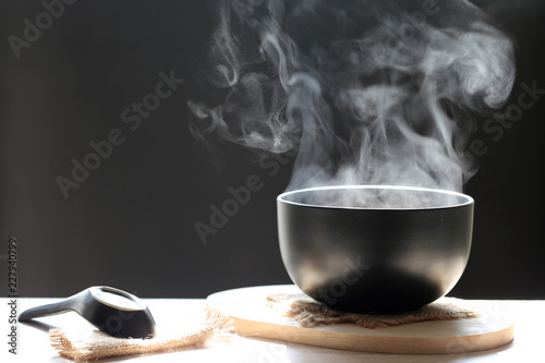 Selective focus of smoke rising with hot soup in cup and spoon on dark background