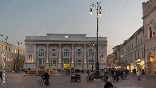 central square of a small town with a fountain in the evening with the passage of people on foot and by bike