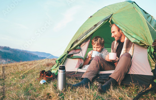 Father with son drink hot tea sitting in camp tent
