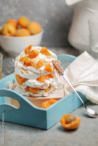 Homemade refined and gentle dessert Pavlova made from meringue, cream and sliced fresh apricots on a blue wooden tray. Close up photo