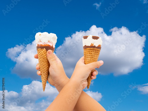 Ice cream cones in hands on blue sky background,