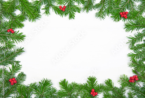 Ghristmas background. Fir branches, red berries on white wooden surface. Frame