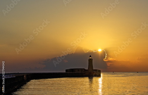 Valletta lighthouse in early orange sunrise light. Romantic sunrise.