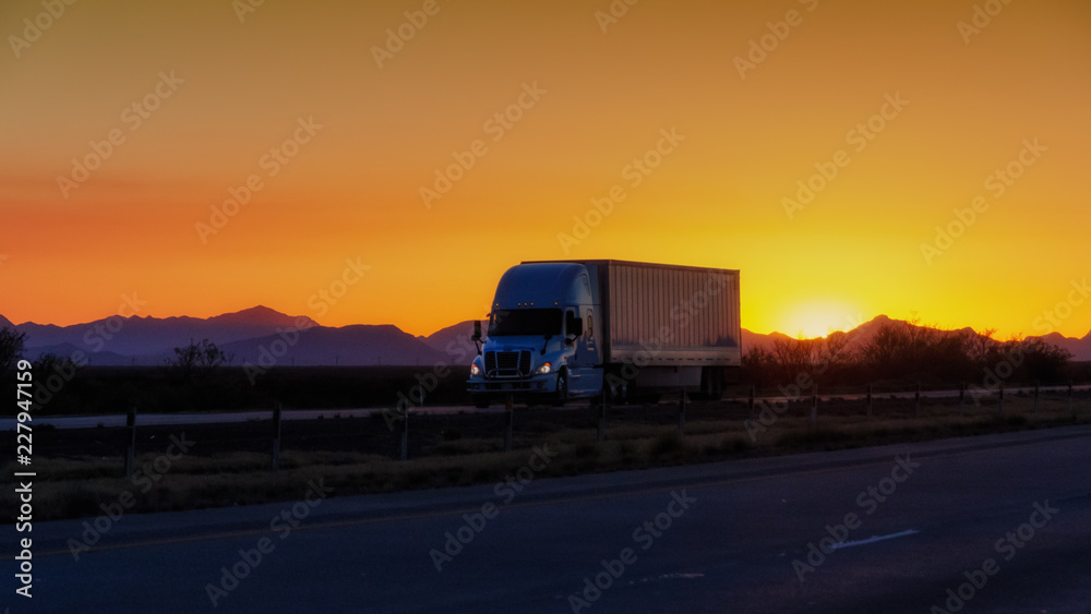 Semi-truck driving on highway at sunset with mountains in background