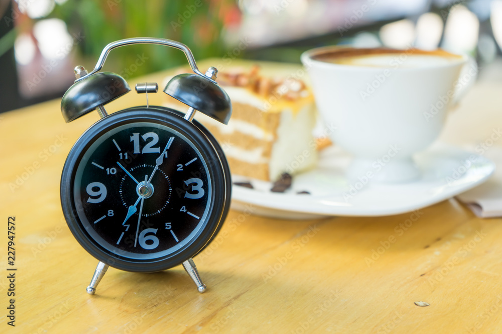 Alarm clock on table with blurred hot coffee background,