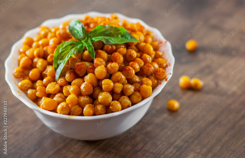 Fried spicy chickpeas in white bowl on wooden table background Fried spicy chickpeas in white bowl on wooden table background