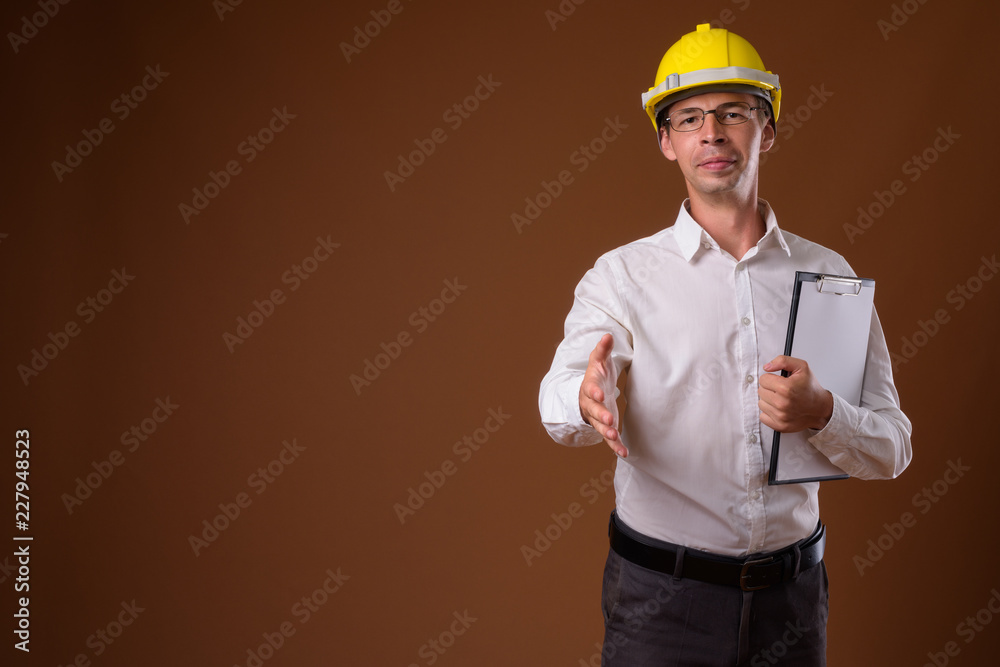 Portrait of businessman wearing hardhat against brown background
