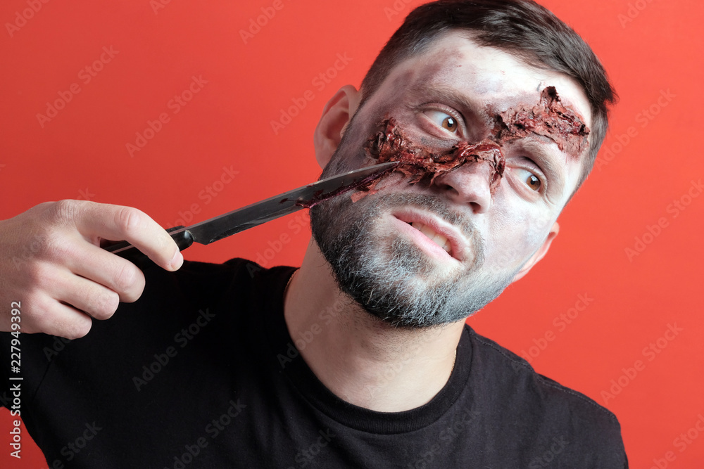 Makeup for halloween party. The bearded guy pretends to cut his face with a  knife. Imitation