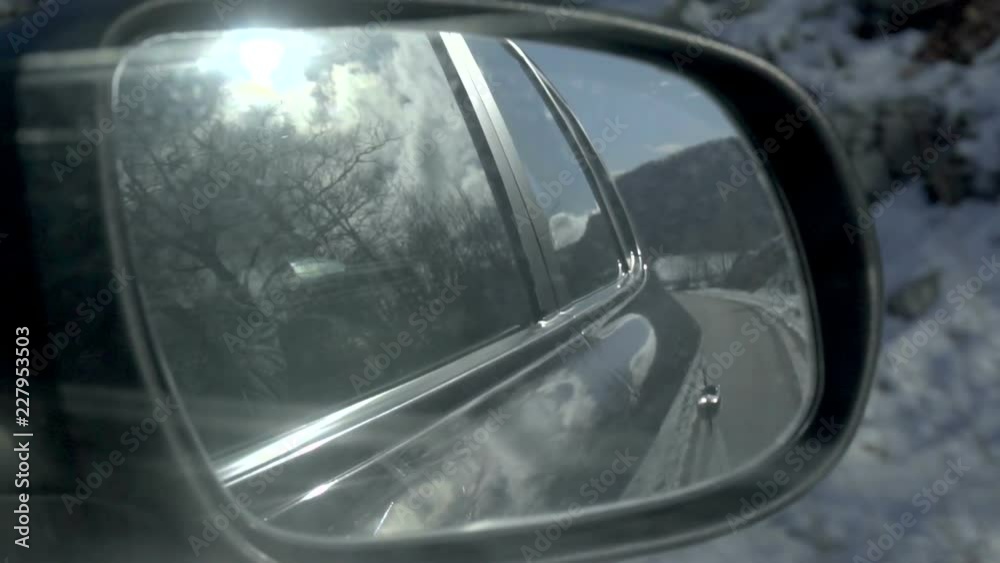 View of the winter road in the rearview mirror of a car. Sun in the clouds