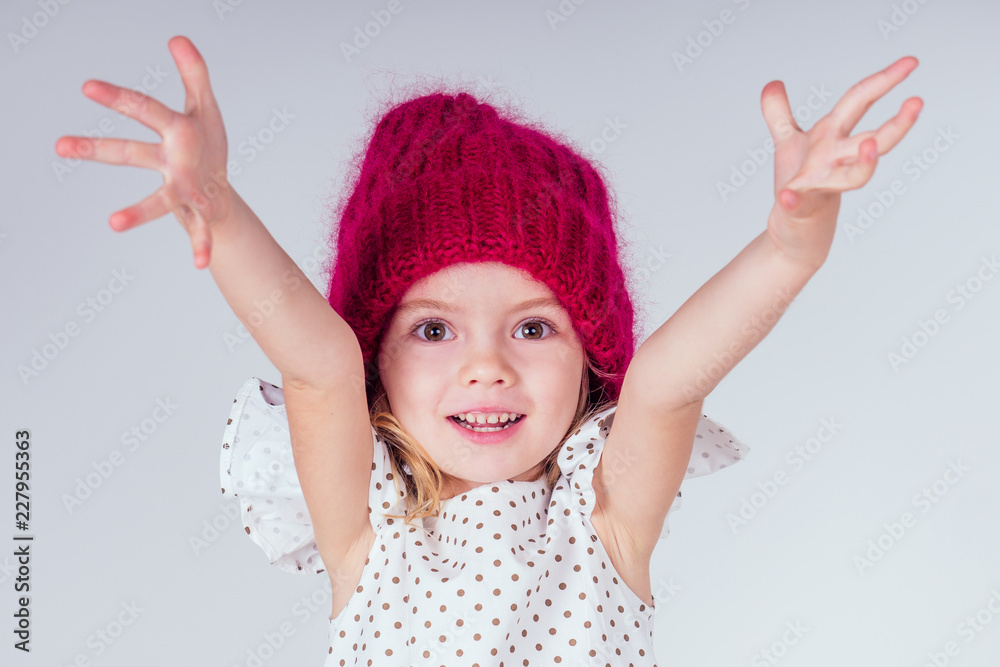 portrait of happy charming little girl wearing knitted red hat and cute white dress on white background in studio. Fashion autumn winter season sale concept.making a wish christmas night and birthday portrait of happy charming little girl wearing knitted red hat and cute white dress on white background in studio. Fashion autumn winter season sale concept.making a wish christmas night and birthday