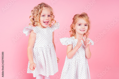 adorable baby amazed and happy smiling birthday party.two little blonde girls twin sisters in a cute white dress in the studio on a pink background,new year Christmas gift.Alice in Wonderland