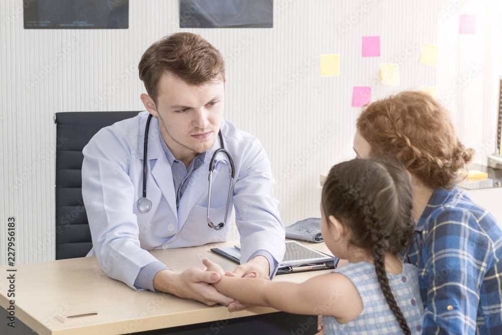 Pediatrician (doctor) man examining,reassuring and discussing child at surgery .Mother Caucasian and kid smiling in hospital room.Copy space. Pediatrician (doctor) man examining,reassuring and discussing child at surgery .Mother Caucasian and kid smiling in hospital room.Copy space.