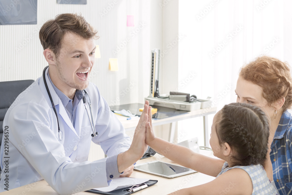 Fototapeta premium Pediatrician (doctor) man giving fist bump (High Five To),reassuring and discussing kid at surgery.Mother Caucasian and kid smiling in hospital room.Copy space.