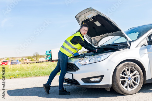 Woman testing car battery in broken car on roadside