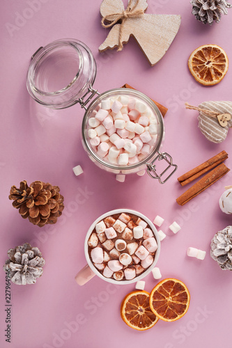 View from above at marshmallows in mug, glass jar and Christmas decoration on pink background