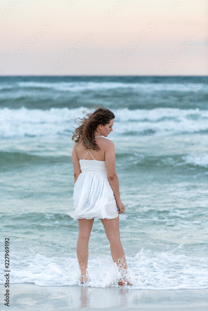 Young woman back standing in white dress on beach sunset in