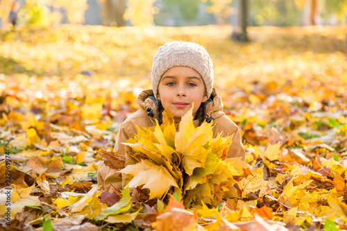 Autumn portrait  Cute little girl lying on the fallen leaves and holding the bouquet of yellow maple leaves in hands