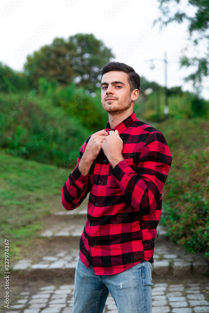 Portrait of stylish male student with bread posing outdoors, looking at camera. Handsome man wearing in red checked shirt walking in autumn park. Concept of study, and mans fashion. Portrait of stylish male student with bread posing outdoors, looking at camera. Handsome man wearing in red checked shirt walking in autumn park. Concept of study, and mans fashion.