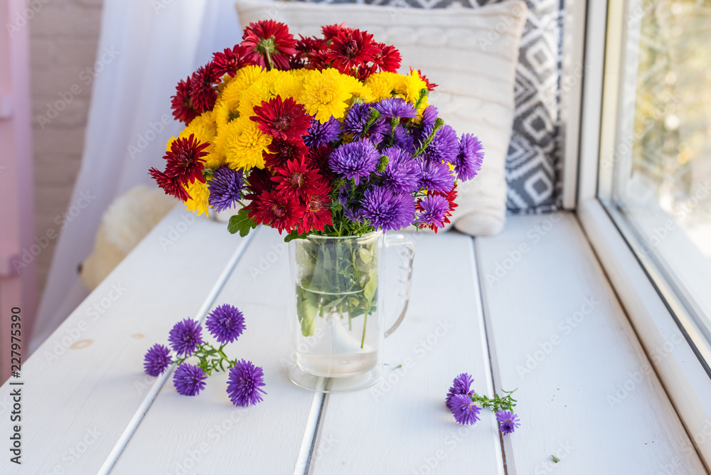 Fototapeta Piękny jasny kolorowy bukiet wielokolorowych kwiatów w szklanym wazonie na drewnianym stole o oknie
