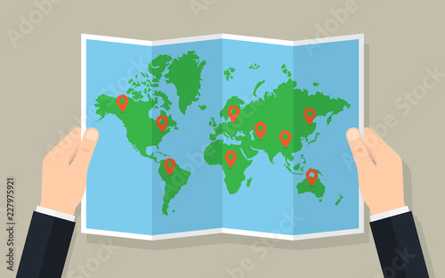 Hands hold folded paper map of world with markers