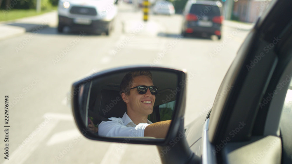 CLOSE UP: Happy young Caucasian man drives through the town on a sunny day.