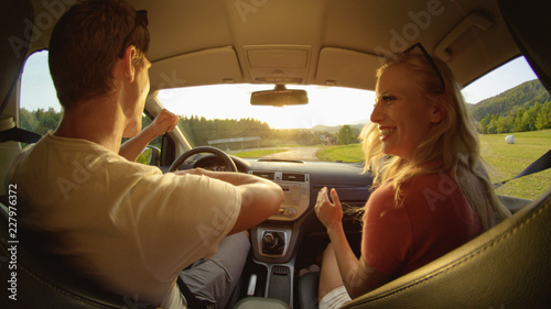 CLOSE UP: Happy young woman and man dance in their car during a scenic cruise.