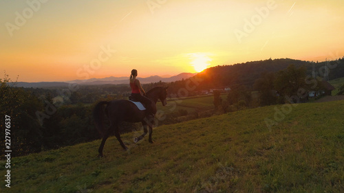 AERIAL: Unrecognizable young woman riding her horse on a scenic sunny evening. © helivideo