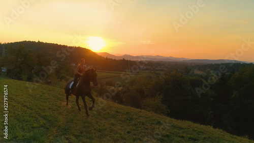 LENS FLARE  Happy young woman galloping on her beautiful horse at idyllic sunset