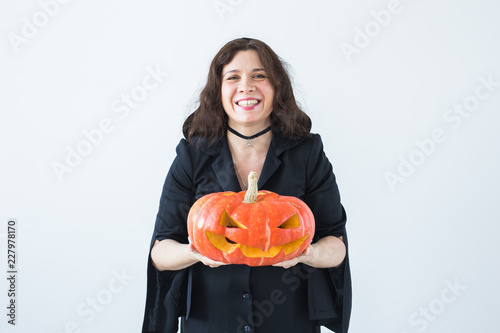 Excited happy young woman in halloween costume posing with carved pumpkin in lightroom
