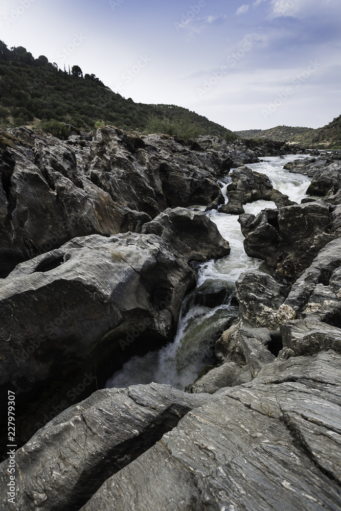 Guadiana river going down between the mountains and rock formations with the cloudy sky in the background