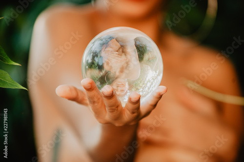 Topless woman holding glass sphere in woods photo