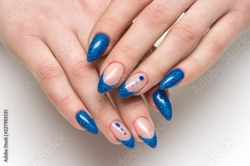 blue french manicure with blue sparkles on long sharp nails with shiny candy on a white background close-up