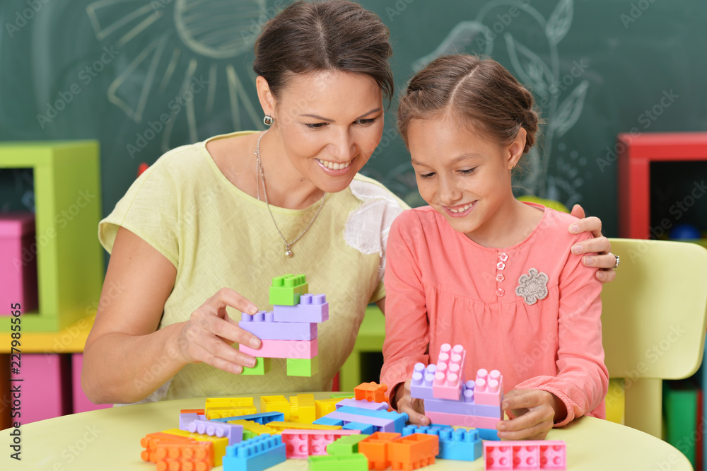 Curly little girl and her mother playing with colorful plastic b Curly little girl and her mother playing with colorful plastic b