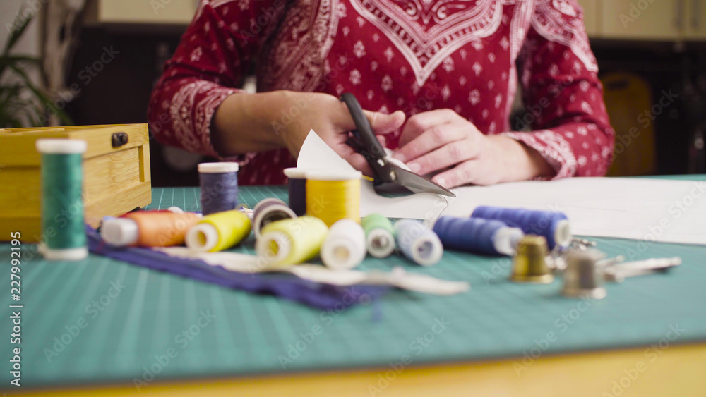 Top view. Middle-age woman hands with scissors cutting paper template. Handmade clothes.